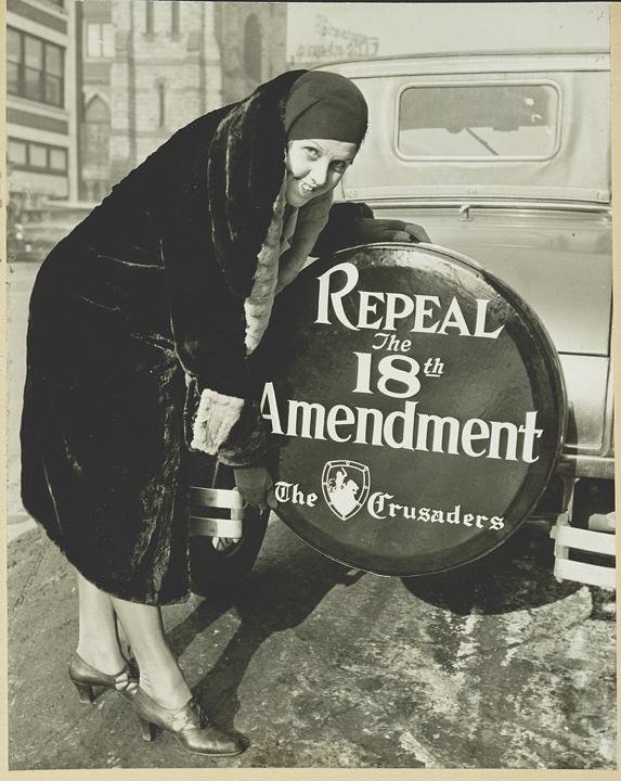 woman standing at the back of a car next to a tire cover that reads repeal the 18th amendment