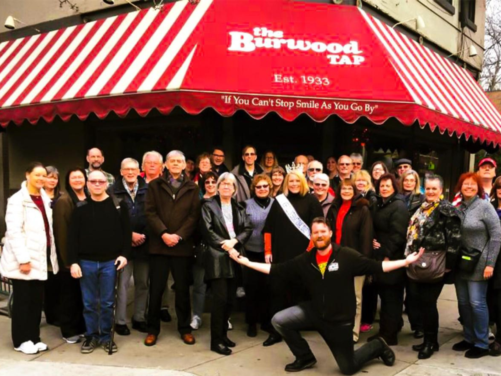 group of people standing outside of the burwood tap with its iconic red and white striped awning